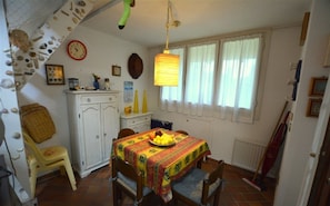 A dining area with a table set for two, a white cabinet, a clock, and a window with curtains.