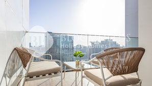 A balcony with two wicker chairs and a small table, a potted plant, and a city view. - Bloomfields Fantastic 1Br In Al Maryah Island (Abu Dabi)