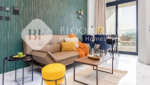 A modern living room with a sofa, coffee table, and chairs. There is a dining area with a table and chairs. A large window provides a view of the outdoors. - Bloomfields Fantastic 1Br In Al Maryah Island (Abu Dabi)