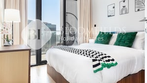 A hotel room with a large bed, a bedside table with a lamp, a view through a large window, and artwork on the wall. - Bloomfields Fantastic 1Br In Al Maryah Island (Abu Dabi)