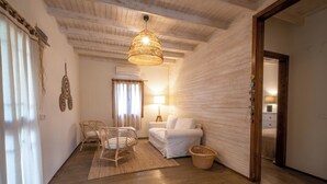 Une pièce chaleureuse avec un plancher en bois, un fauteuil en osier, un canapé blanc, une lampe et un panier.