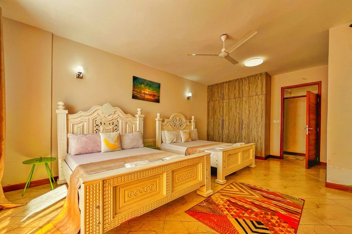 A hotel room with two beds, a ceiling fan, a painting, and a wooden wardrobe.
