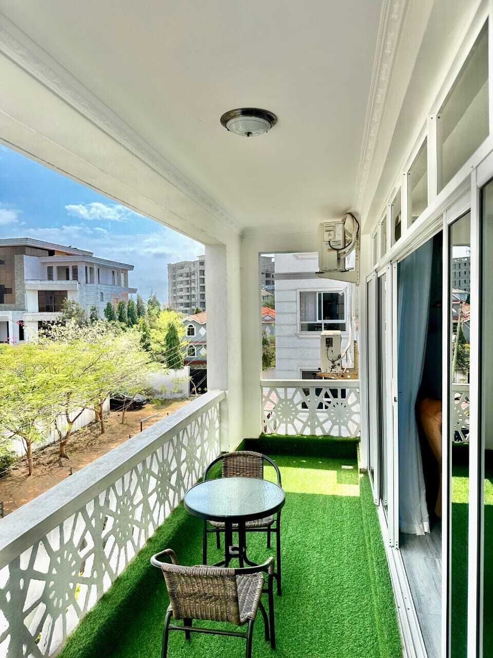 A balcony with a table and chairs, a white railing, and a view of buildings and trees.
