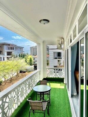 A balcony with a table and chairs, a white railing, and a view of buildings and trees. - Nyali Luxury Apartments Antalya (Mombasa)