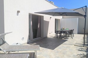 A patio with a table and chairs, a sun lounger, and a large umbrella. - Tesino Green – Eco Stay with Beach Access (Grottammare)
