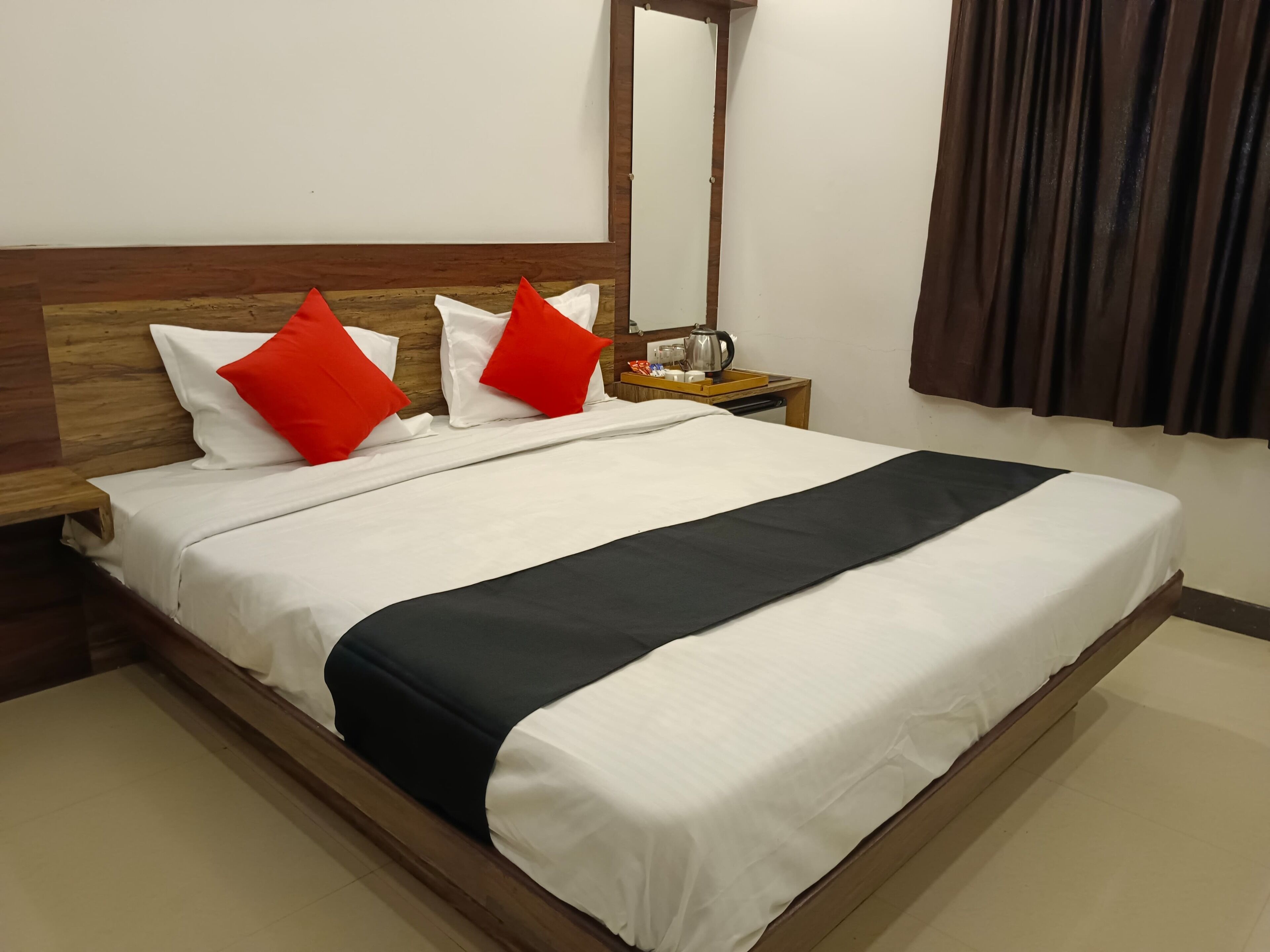 A neatly made bed with white and black bedding, two red pillows, and a wooden headboard.