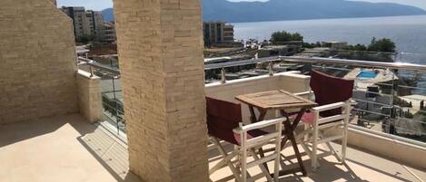 A balcony with a table and chairs, overlooking a body of water and distant mountains.