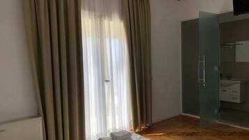A hotel room with a bed, a bathroom with a glass door, and curtains on the window.