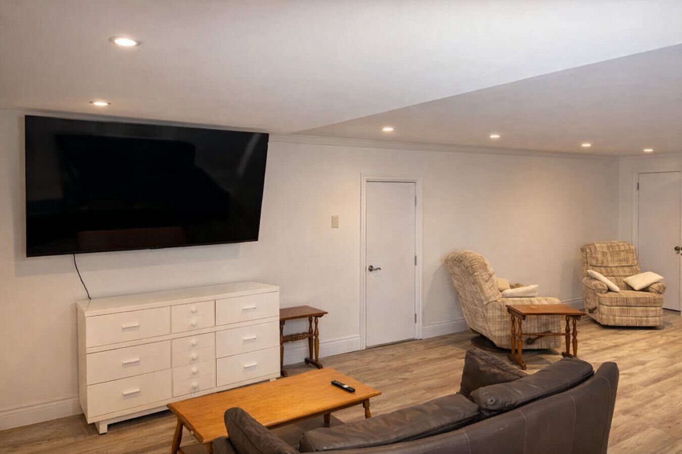 A living room with a flat-screen TV, a sofa, a coffee table, a cabinet, and two armchairs.