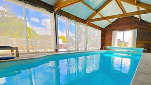 Une piscine intérieure avec des parois en verre transparent, des poutres en bois et un banc.