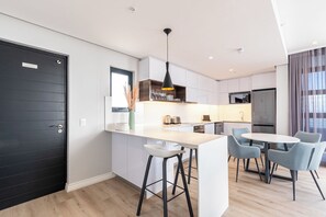 A modern kitchen with white cabinets, a black door, and a central island with bar stools. - 16 On Bree Superior Apartment (Cape Town)