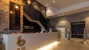 Un comptoir d’accueil avec un mur en pierre, un escalier et un ascenseur moderne.
