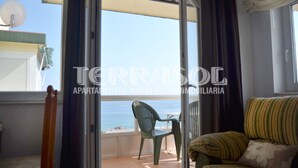 A balcony with a view of the sea, a green chair, and a striped sofa.