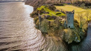 Eine historische Burgruine an einem See unter blauem Himmel.