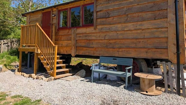 Eine Holzhütte mit einer Holztreppe, die zu einer roten Tür führt, einer Bank und einer Spule Seil.