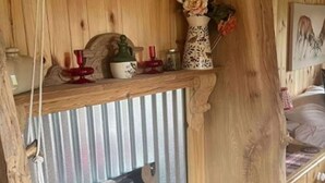 Ein rustikaler Holzinnenraum mit einem schwarzen Holzofen, einer Ablage mit Dekorationen und einer Holztür.