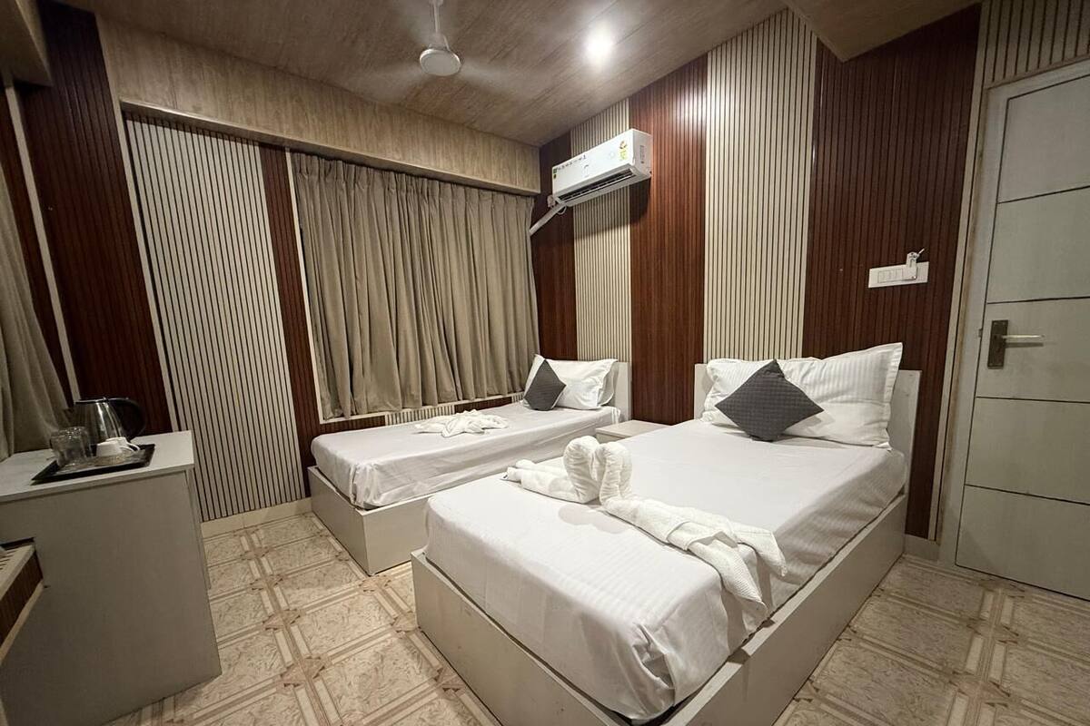 Una habitación de hotel con dos camas individuales, un escritorio pequeño con una tetera y un armario.
