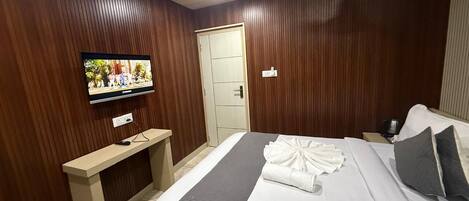 A hotel room with a bed, a TV mounted on the wall, a desk, and a door.