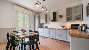 A modern kitchen with white cabinets, a wooden dining table, and black chairs. There is a window providing natural light and a clock on the wall. - Cosy apartment for 6 guests with A/C, private pool, WIFI, TV and terrace (Casarza Ligure)