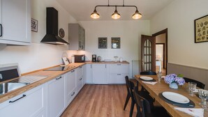 A modern kitchen with white cabinets, a wooden countertop, and a dining area with a wooden table set for two. - Cosy apartment for 6 guests with A/C, private pool, WIFI, TV and terrace (Casarza Ligure)