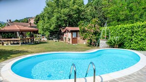 A swimming pool with stone tiles, surrounded by a grassy area and trees. - Cosy apartment for 6 guests with A/C, private pool, WIFI, TV and terrace (Casarza Ligure)