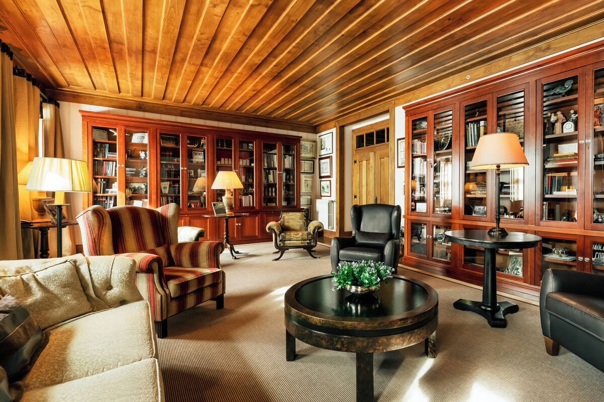 A library with bookshelves, leather armchairs, a coffee table, and lamps.