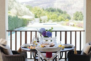 A dining table set outdoors with a view of a pool and greenery. - Casas da Memória (Tarouca)