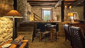 A rustic interior with stone walls, wooden beams, a dining table with chairs, and a ship model. - Casas da Memória (Tarouca)