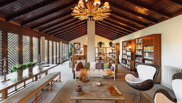 A spacious room with a high ceiling, wooden beams, a central chandelier, a sofa set, a coffee table, and a bookshelf. - Casas da Memória (Tarouca)