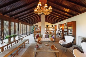 A spacious room with a high ceiling, wooden beams, a central chandelier, a sofa set, a coffee table, and a bookshelf. - Casas da Memória (Tarouca)