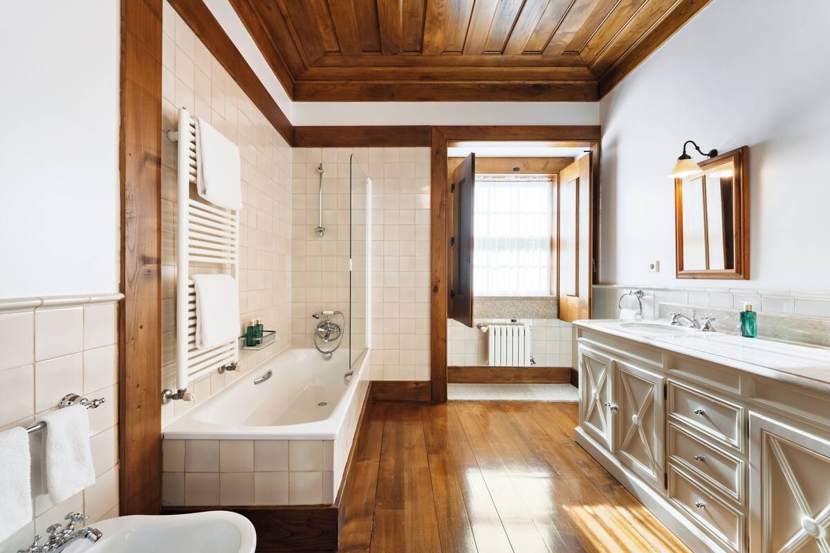 A bathroom with a bathtub, a sink, a mirror, and wooden flooring.