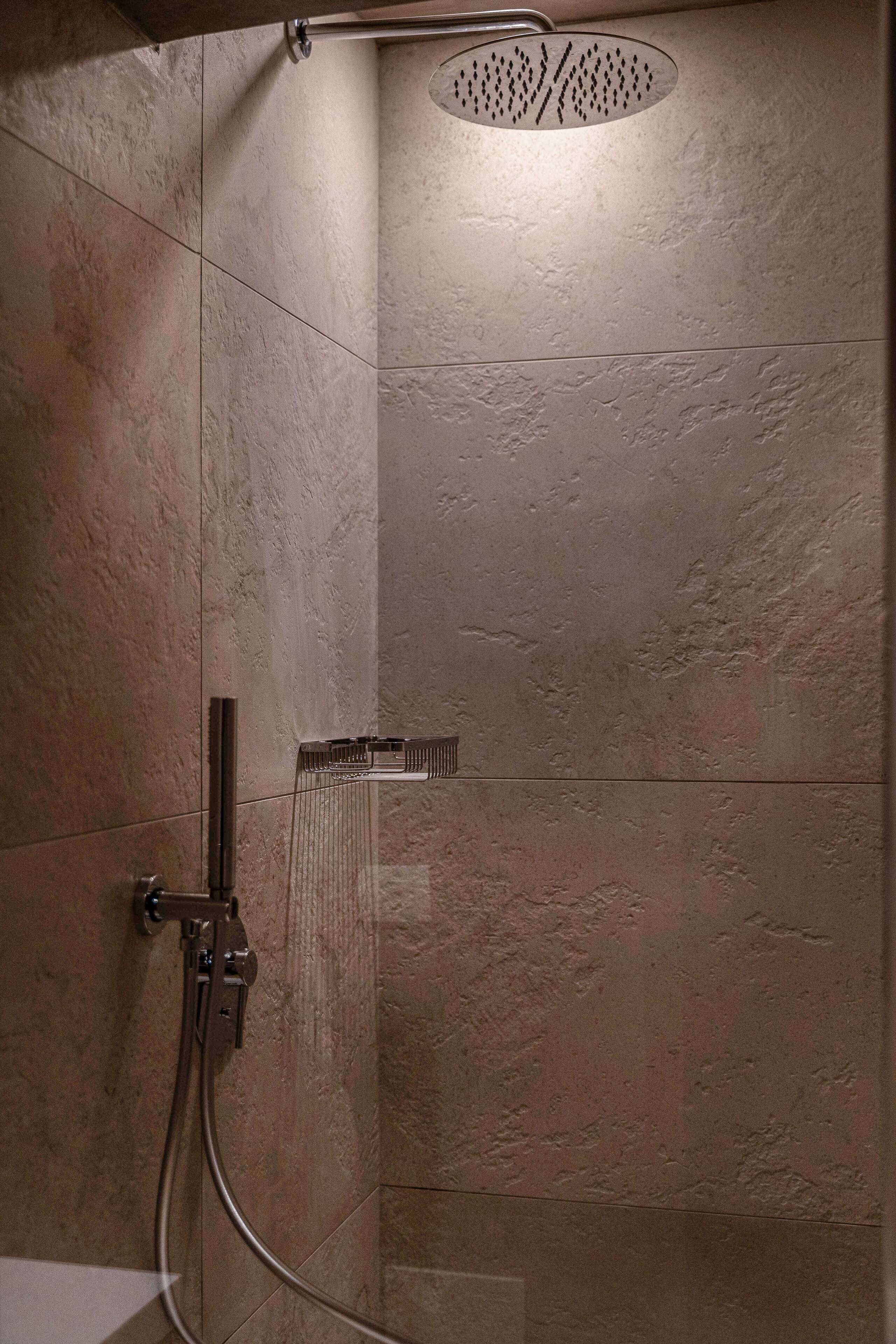 Una ducha con cabezal de ducha de mano y panel de control en la pared.