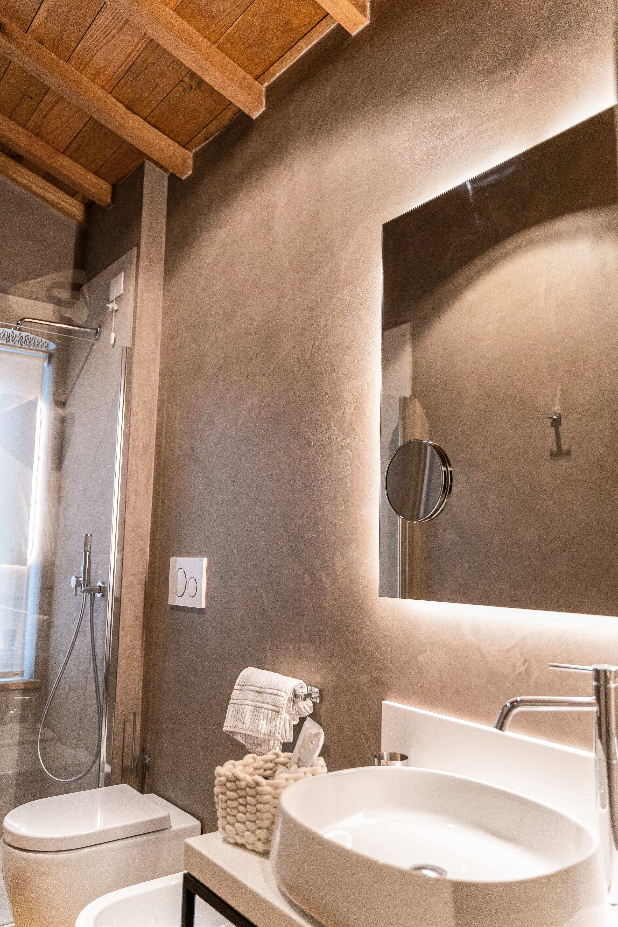 Une salle de bain avec un plafond en bois, un grand miroir, un lavabo blanc et une douche.