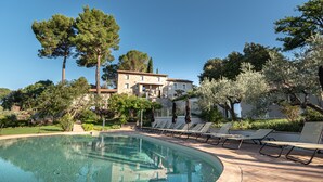 Una piscina con lettini e ombrelloni, circondata da alberi e un edificio.