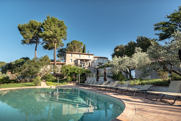 A swimming pool with lounge chairs and umbrellas, surrounded by trees and a building. - Sogno di Davide Country House (Assisi)