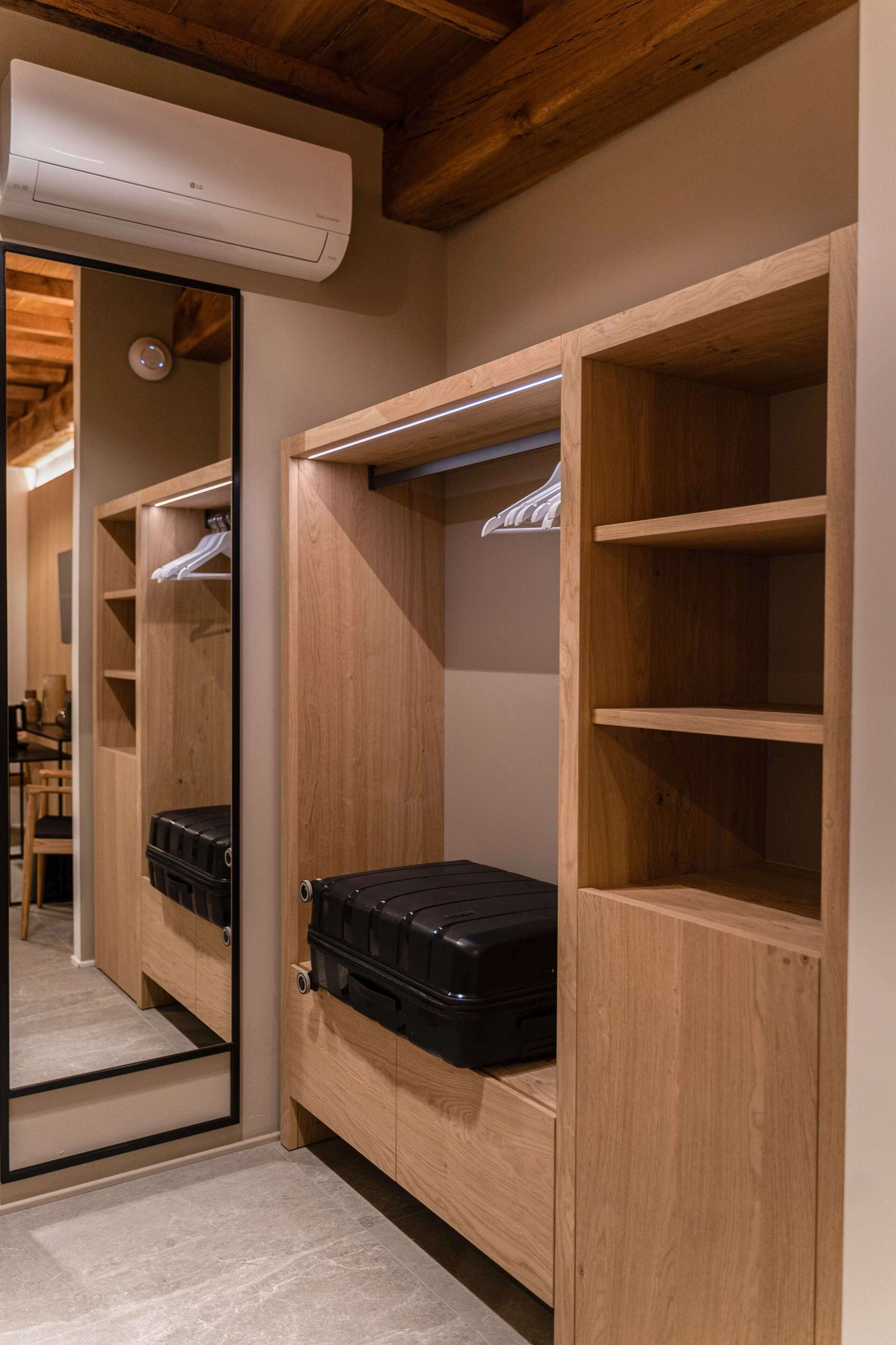 A walk-in closet with wooden shelving, a mirrored closet door, and a black suitcase.