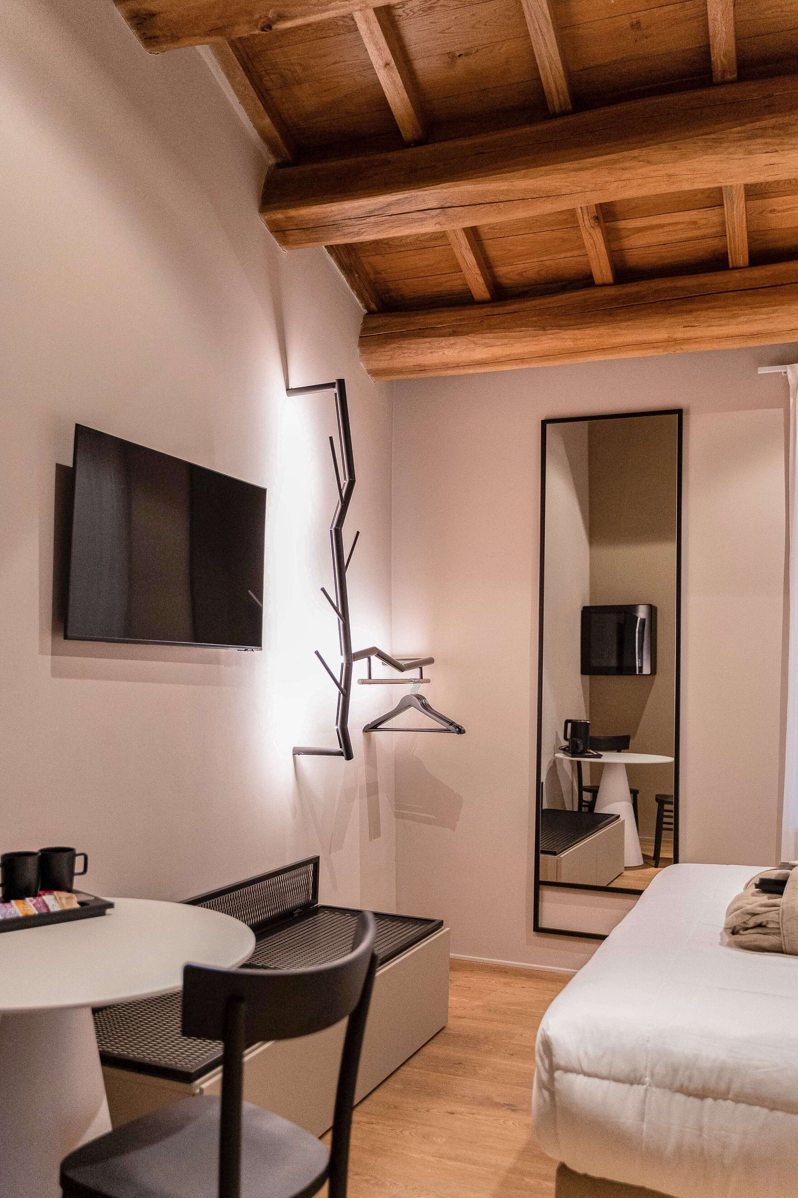 Een kleine hotelkamer met een bed, een bureau met stoel, een televisie en een spiegel.