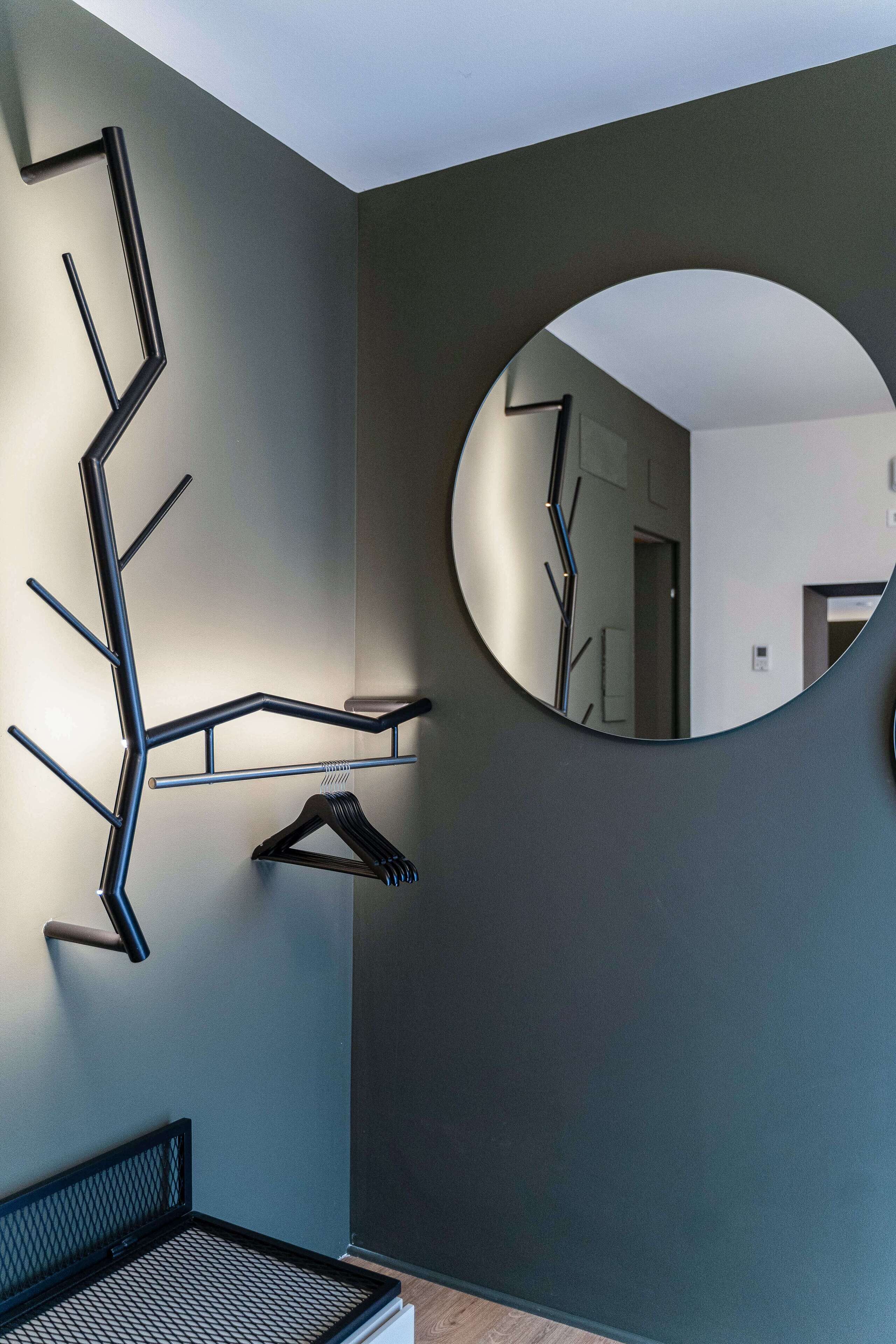 A modern room with a wall-mounted coat rack, a round mirror, and a bed with a metal frame.