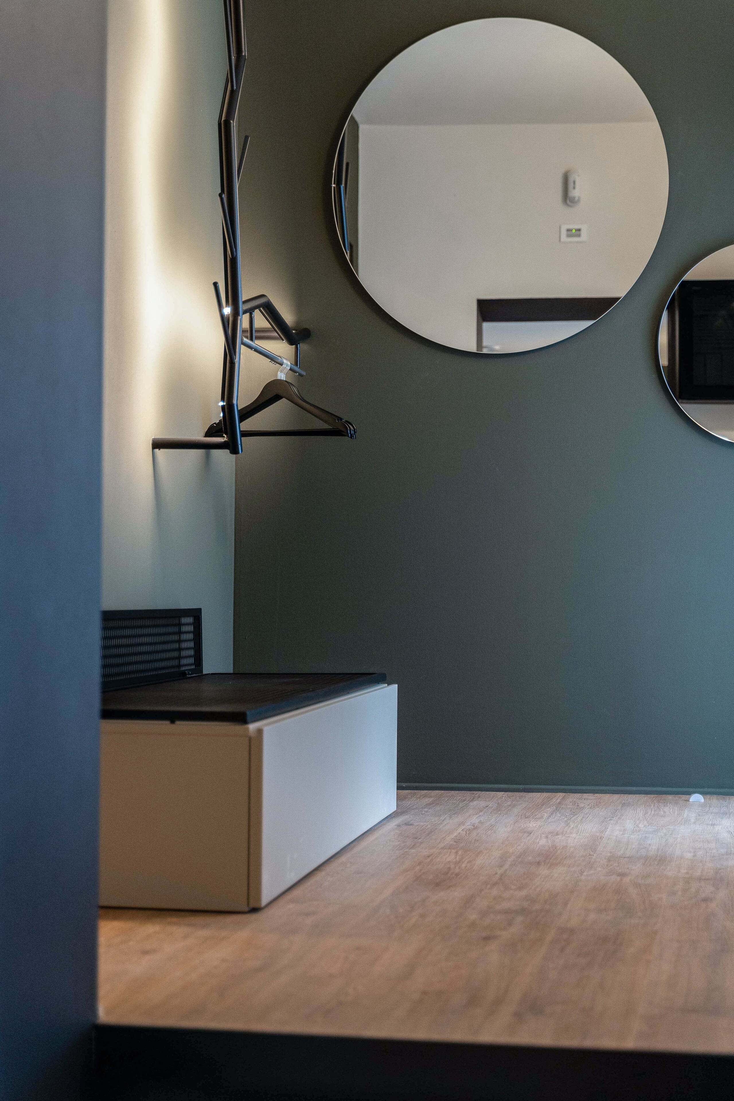 A modern room with a wooden floor, a black desk, a white cabinet, and two round mirrors on the wall.