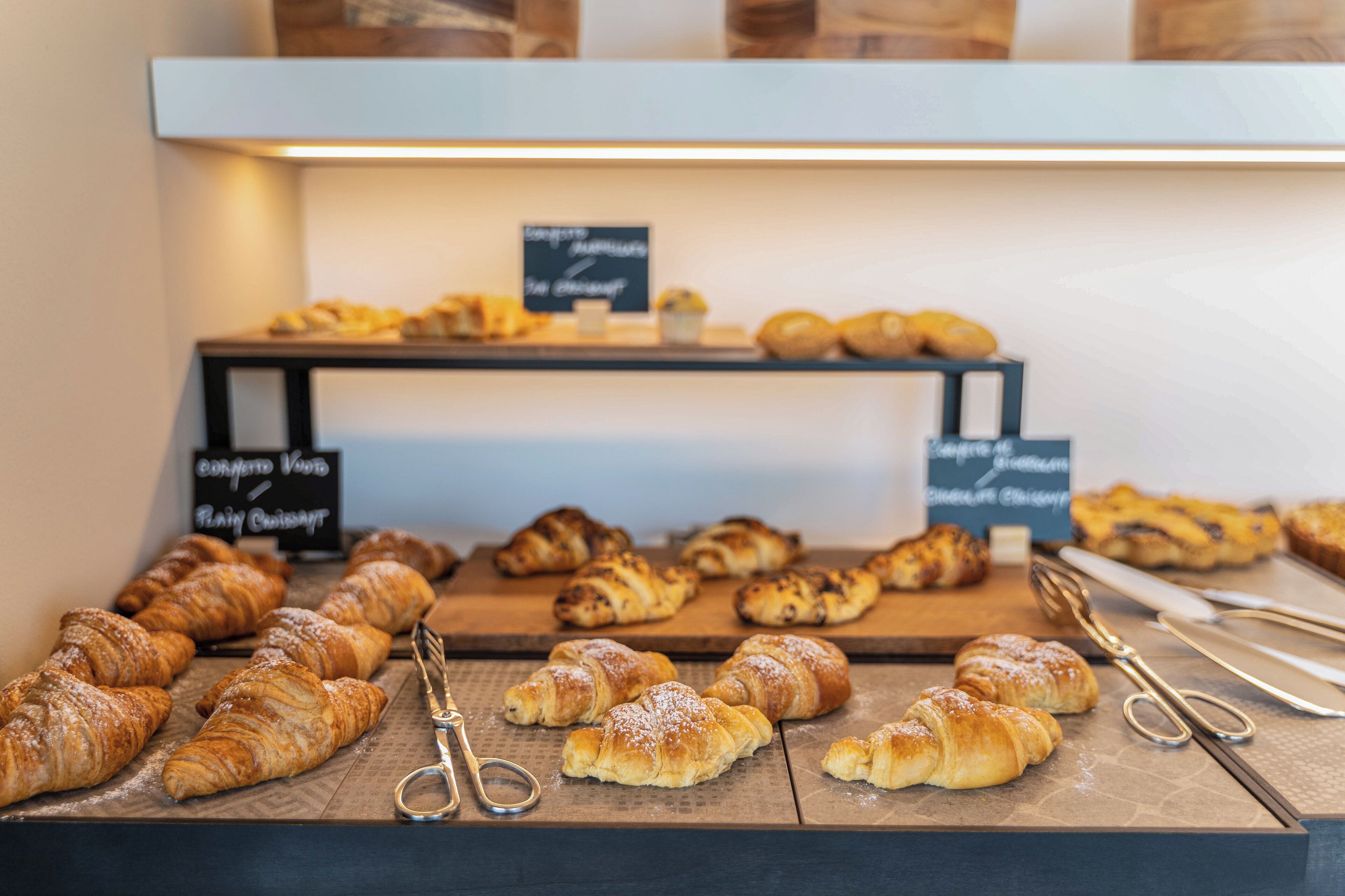 A display of assorted pastries and croissants on wooden boards, with signs indicating different types of baked goods.