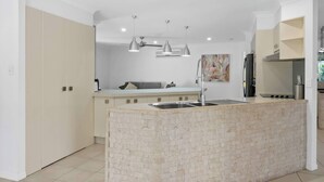A modern kitchen with a central island, pendant lighting, and a built-in oven. - Haven by Khove (Pacific Pines)
