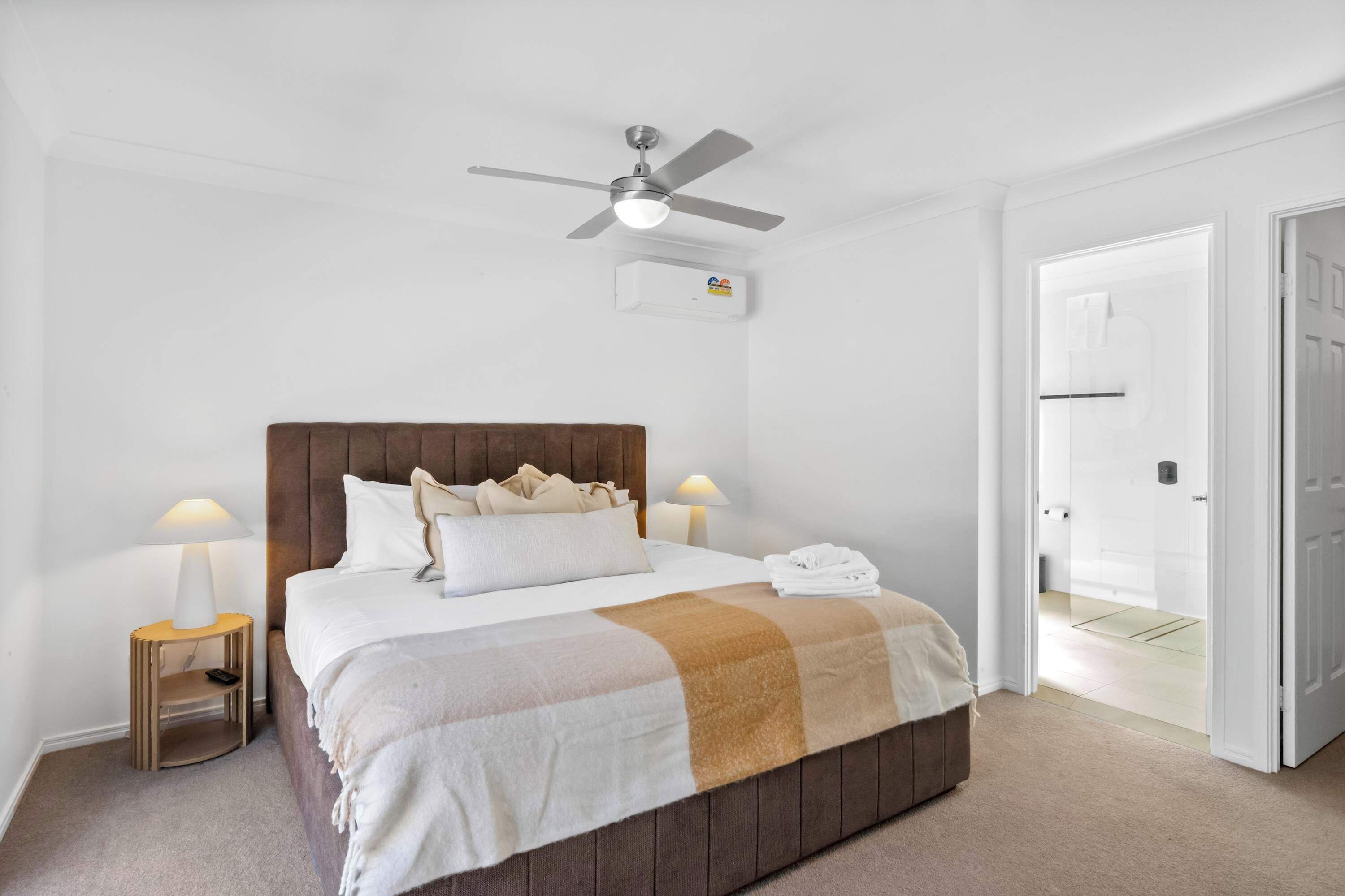 A hotel room with a bed, bedside lamps, a ceiling fan, and a door leading to another room.