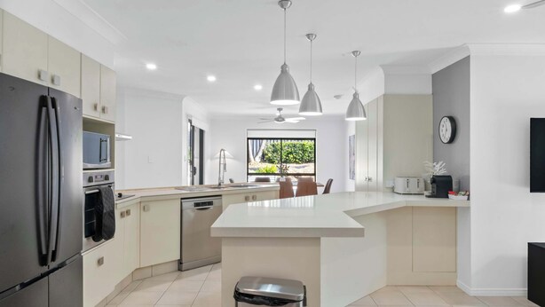 A modern kitchen with a central island, stainless steel appliances, pendant lighting, and a view to the outdoors. - Haven by Khove (Pacific Pines)