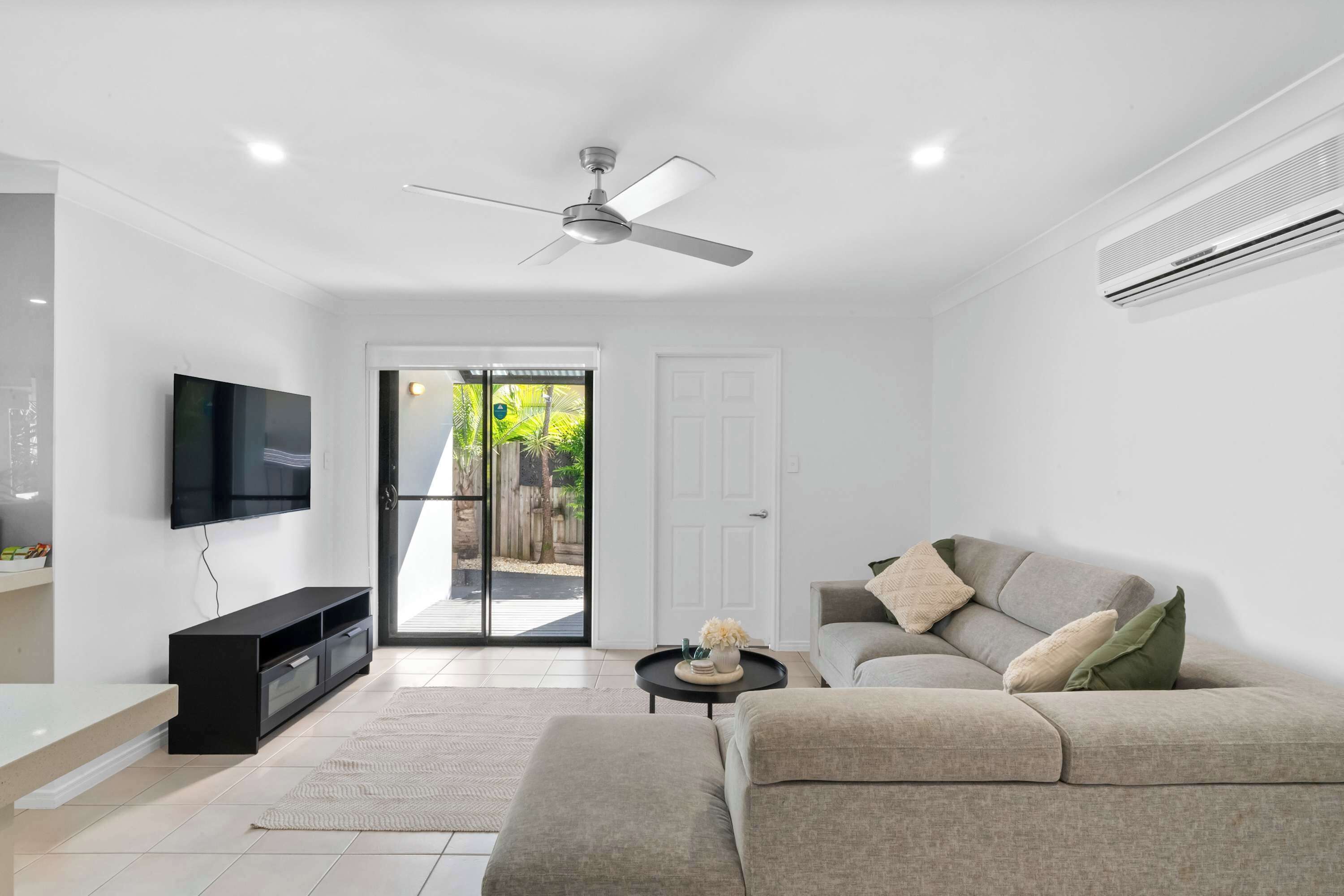 A modern living room with a flat-screen TV, a ceiling fan, a sofa, and a small coffee table.