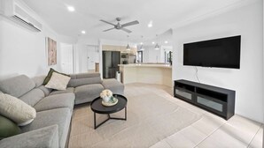 A modern living room with a grey sofa, a black coffee table, and a flat-screen TV mounted on the wall. - Haven by Khove (Pacific Pines)