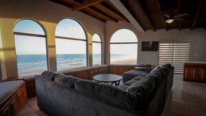 Un salón con un sofá grande de color gris, una mesita redonda y vistas a la playa a través de ventanales abovedados.