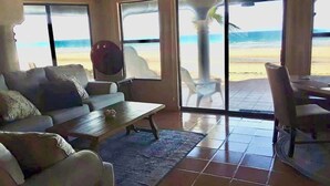 Una sala de estar con sofá, una mesa de centro y vista a la playa a través de amplias ventanas.