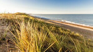 Une plage avec un ciel dégagé, un sentier sablonneux et de l’herbe au premier plan.
