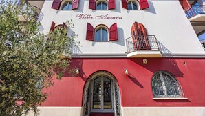 Ein Gebäude mit roter und weißer Fassade, gebogenen Fenstern und Balkonen mit roten Fensterläden.