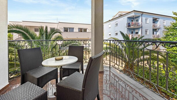 Ein Balkon mit Korbmöbeln, einem kleinen runden Tisch und Blick auf ein Gebäude mit Balkonen.